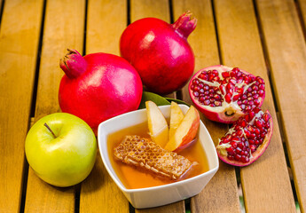 Traditional foods of Rosh HaShana - Jewish New Year: a bowl of honey with the honeycomb,  apples and pomegranates; on wooden background
