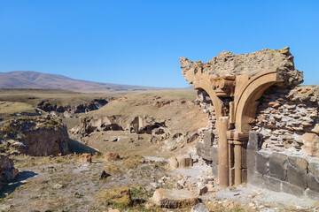 Broken stone arch & walls on edge of medieval city Ani, near Kars, Turkey. Caved gorge, surrounding city is on background. City was founded in 5 century by Armenians. Now it's included in UNESCO