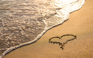 A heart is drawn on the sandy beach. The sea wave washes the beach at sunset.