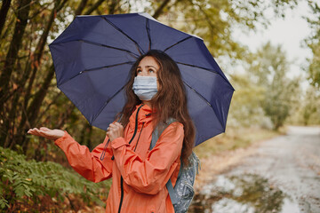 Young caucasian woman in a coronavirus mask holding an umbrella while resting in the autumn forest...