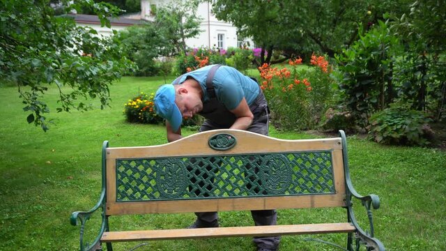 Gardener man disassemble retro bench in garden yard. Outdoor furniture renew