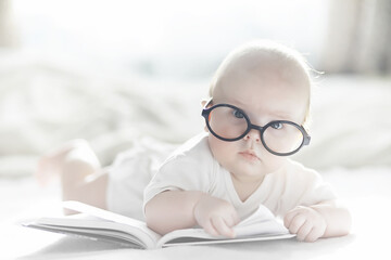A newborn baby is lying on a soft bed in glasses.