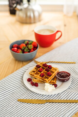 Belgian waffles for breakfast. Waffles with fresh berries and berry jam. Cup of coffee and teapot on the table. Breakfast in the trailer