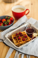 Belgian waffles for breakfast. Waffles with fresh berries and berry jam. Cup of coffee and teapot on the table. Breakfast in the trailer