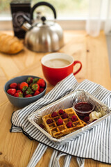 Belgian waffles for breakfast. Waffles with fresh berries and berry jam. Cup of coffee and teapot on the table. Breakfast in the trailer