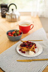 Belgian waffles for breakfast. Waffles with fresh berries and berry jam. Cup of coffee and teapot on the table. Breakfast in the trailer