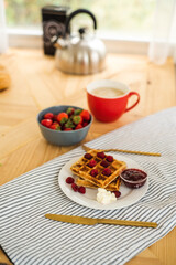 Belgian waffles for breakfast. Waffles with fresh berries and berry jam. Cup of coffee and teapot on the table. Breakfast in the trailer