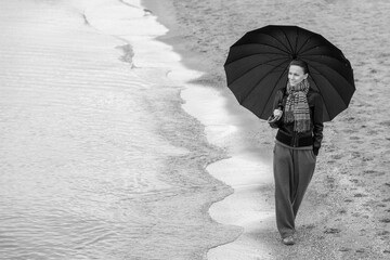 woman with umbrella in winter or autumn walking near sea