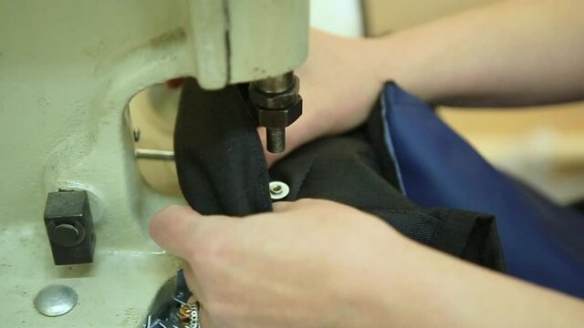 Closeup view of Hands of Young Girl of sewer attaching metal round snaps to clothes with help of special machine at garment factory. Male worker using press for installing eyelet on leather product