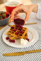 Poured with jam Belgian waffles for breakfast. Waffles with fresh berries and berry jam. Cup of coffee and teapot on the table. Breakfast in the trailer