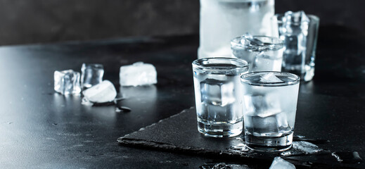 Vodka in shot glasses on black stone background, iced strong drink in misted glass