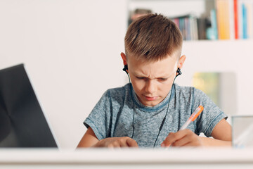 Young boy in headset sitting at table with laptop and preparing to school at home. Online education concept.