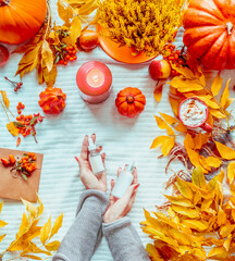 Women hands holding bottles of cosmetic products on white blanket with pumpkins, candles and fall...