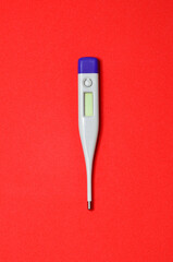 Electronic thermometer for temperature measurement isolated on a red background with space for text or design top view