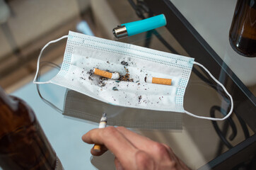 People drinking beer and smoking cigarette using a mask as an ashtray.