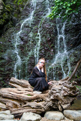 Young girl in black posing squatting on a large dry tree against the background of a mountain...