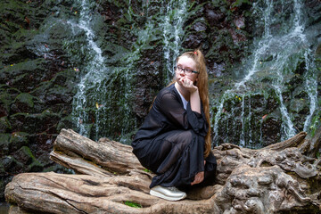 Young girl in black posing squatting on a large dry tree against the background of a mountain...