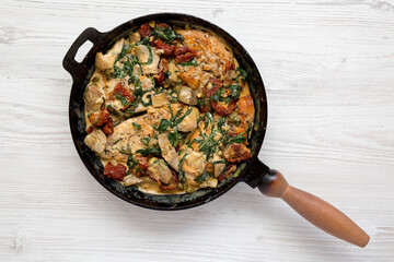 Homemade Creamy Tuscan Chicken in a cast iron pan on a white wooden background, top view. Flat lay, overhead, from above.