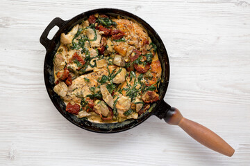 Homemade Creamy Tuscan Chicken in a cast iron pan on a white wooden background, top view. Flat lay, overhead, from above.