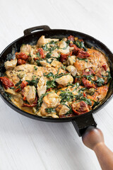 Homemade Creamy Tuscan Chicken in a cast-iron pan on a white wooden surface, low angle view.