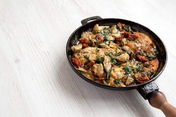 Homemade Creamy Tuscan Chicken in a cast-iron pan on a white wooden surface, low angle view. Space for text.