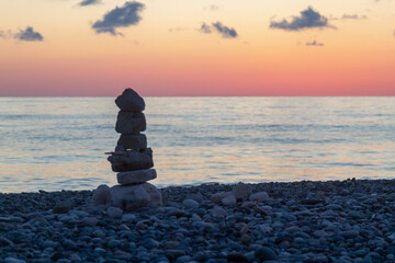 Composition of balancing stones on the pebbly coast of the Black Sea against the background of sunset