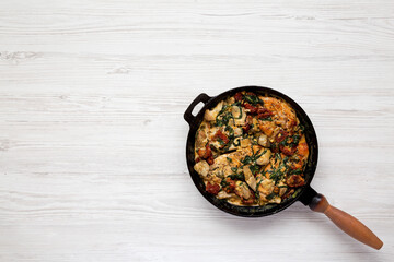 Homemade Creamy Tuscan Chicken in a cast-iron pan on a white wooden background, top view. Flat lay, overhead, from above. Space for text.