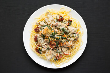 Homemade Creamy Tuscan Chicken with Pasta on a white plate on a black background, side view. Close-up.