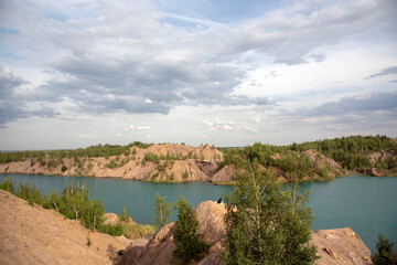 Blue lake among the sand hills on the textured background of the cloudy sky.