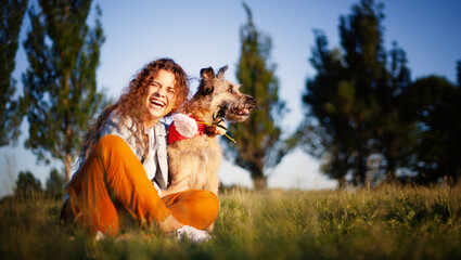 Young curly joyful smiling beautiful woman with her dog in the park on green grass