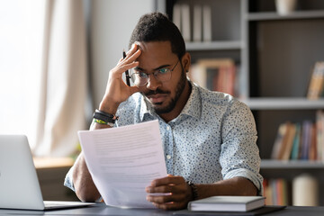 African American man wearing glasses dissatisfied by bad news received in letter, holding document,...
