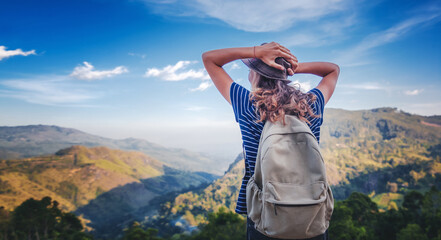Young female traveler with a backpack and in a hat admiring enjoying the beautiful mountain landscape, travel and freedom lifestyle - obrazy, fototapety, plakaty