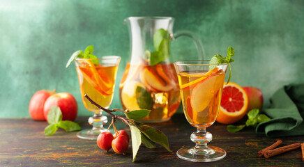 Apple cider cocktail with red oranges and spices in glasses and jug on table. Concept of autumn and winter drinks.