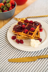 Belgian waffles for breakfast. Waffles with fresh berries and berry jam. Cup of coffee and teapot on the table. Breakfast in the trailer