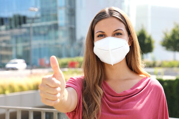 COVID-19 Optimistic business woman wearing protective mask KN95 FFP2  showing thumbs up in modern...