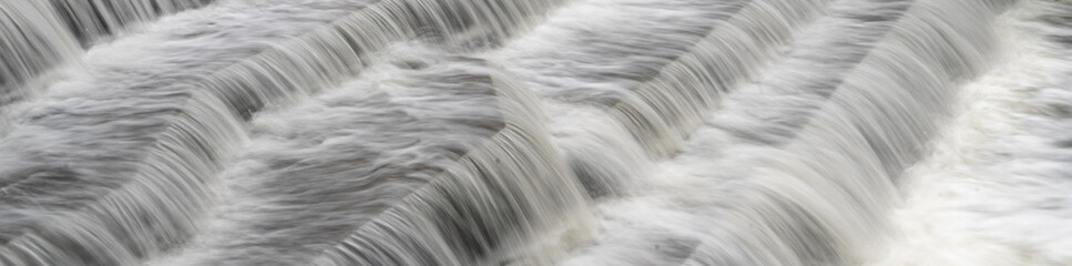 Fototapeta na wymiar White Water flowing over weir low-level view at long exposure for blurred water effects and textures 