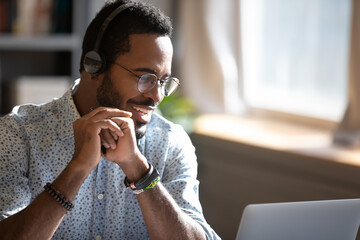 Smiling African American man wearing headphones speaking close up, using laptop, looking at screen,...