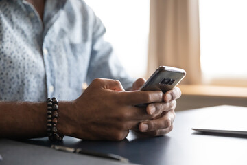 Close up African American man using phone, sitting at work desk, young male hands holding...