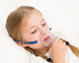 girl is breathing through an inhaler. a sick child is lying on the bed