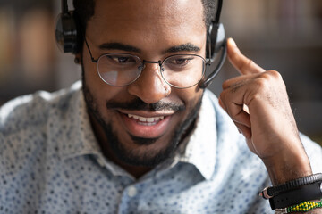 Close up friendly African American man wearing headset speaking in microphone, smiling call center...