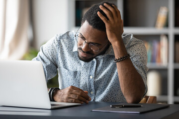 Upset stressed African American businessman using laptop, frustrated unhappy young man wearing...