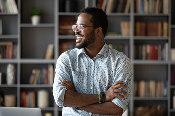 Smiling positive African American young man wearing glasses dreaming about good future and...