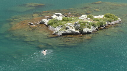 Hombre nadando hacia pequeña isla con aguas cristalinas