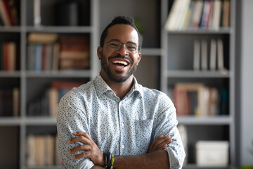 Head shot portrait laughing excited African American man wearing glasses standing with arms crossed...