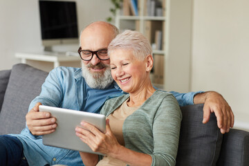 Happy senior couple sitting on sofa and watching movie on digital tablet at home
