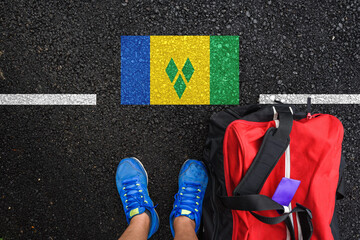 a man with a shoes and travel bag is standing on asphalt next to flag of Saint Vincent and the...