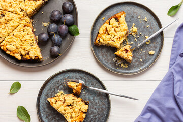Delicious juicy dessert on a white wooden background, portions of plum pie in a plate with a fork