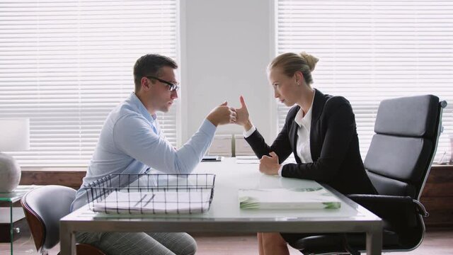 male and female office workers sit at table face to face. finger wrestling fight and competition, tense struggle between two managers. look resolute, determined. humorous equal rights concept