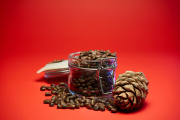 4k. Pine nuts spilled out of a glass jar on red background. Close up.