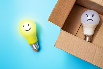 Yellow light bulb with face is outside the box while white bulb is inside the box on blue backgroud , think outside the box concept